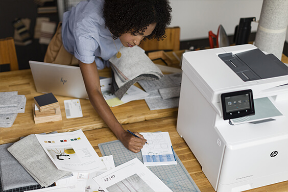 woman bending over desk working on printed material from HP printer